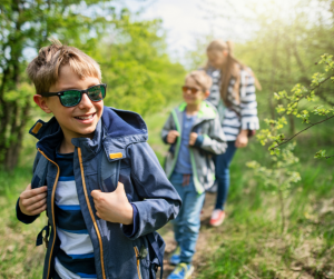 Three kids hiking through a green forest on a clear spring day