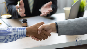 Two people are shaking hands over a table in the presence of a third party mediator